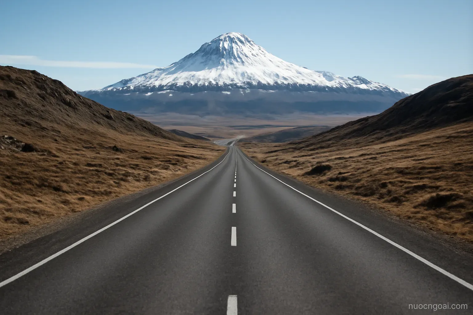 A high stony plateau under a snow-capped peak, a straight road between bare hills in clear cold light