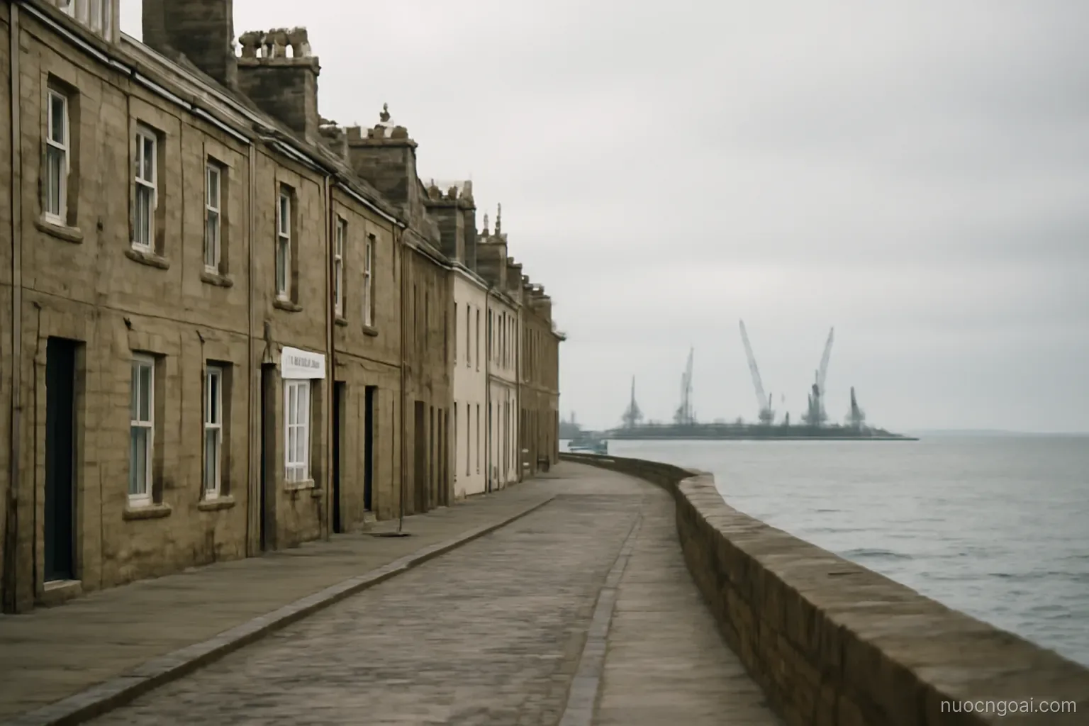 An oil-era seafront of stone facades facing a flat grey inland sea, cranes and derricks on the far spit