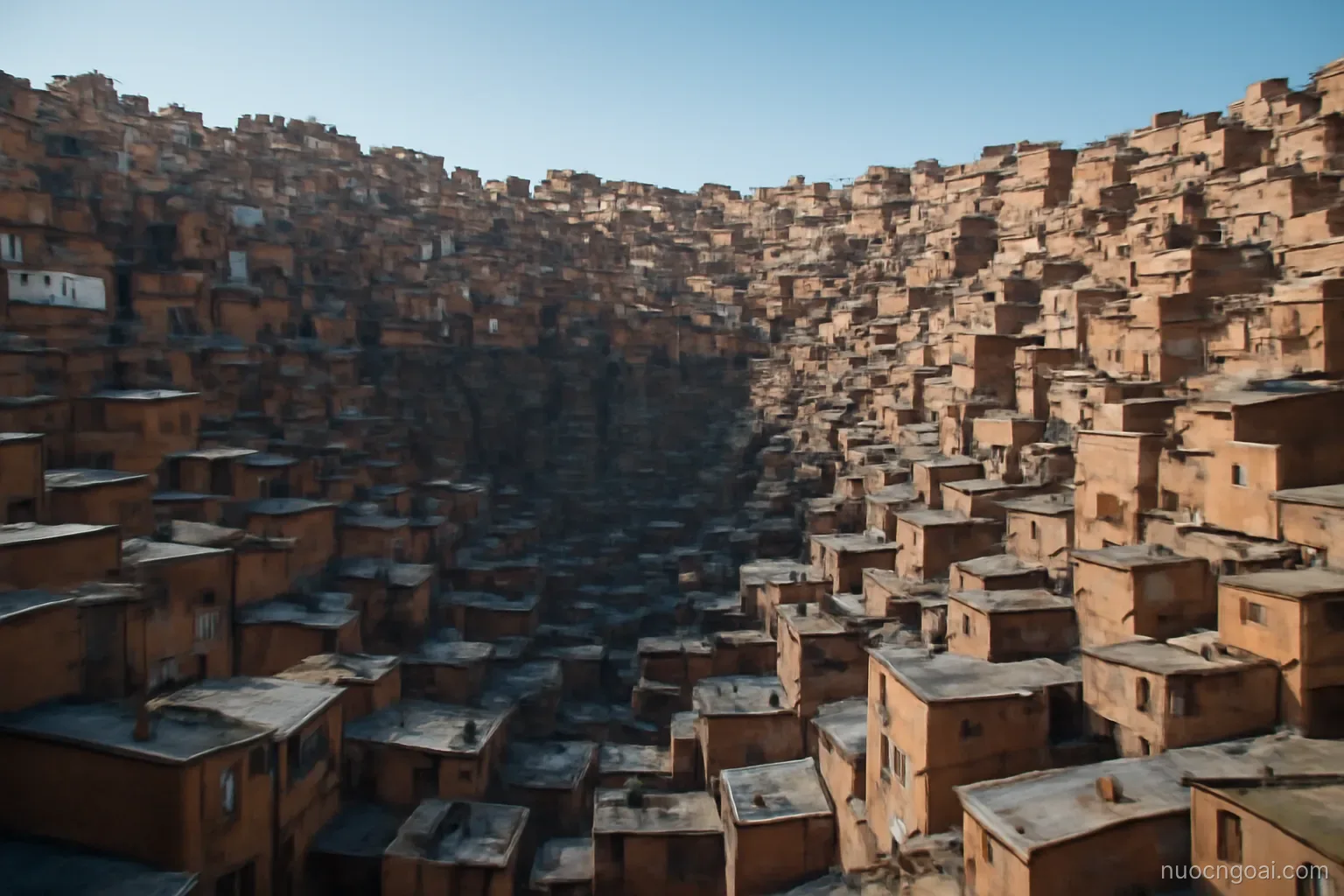 A city spilling down the walls of a deep basin, brick houses stacked to the rim under thin blue sky