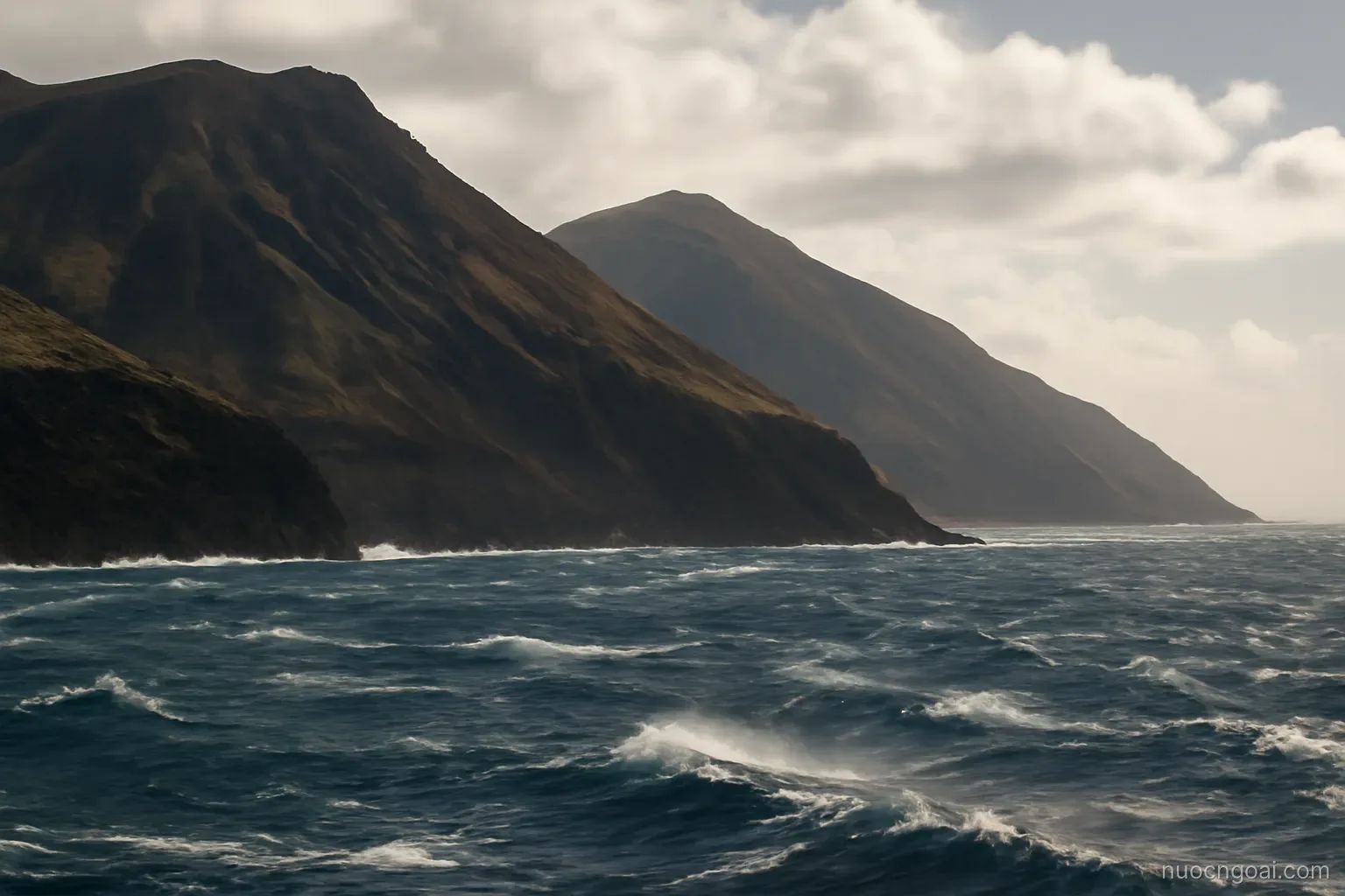 Steep volcanic slopes above an open Atlantic bay with whitecaps driven hard across the water by wind