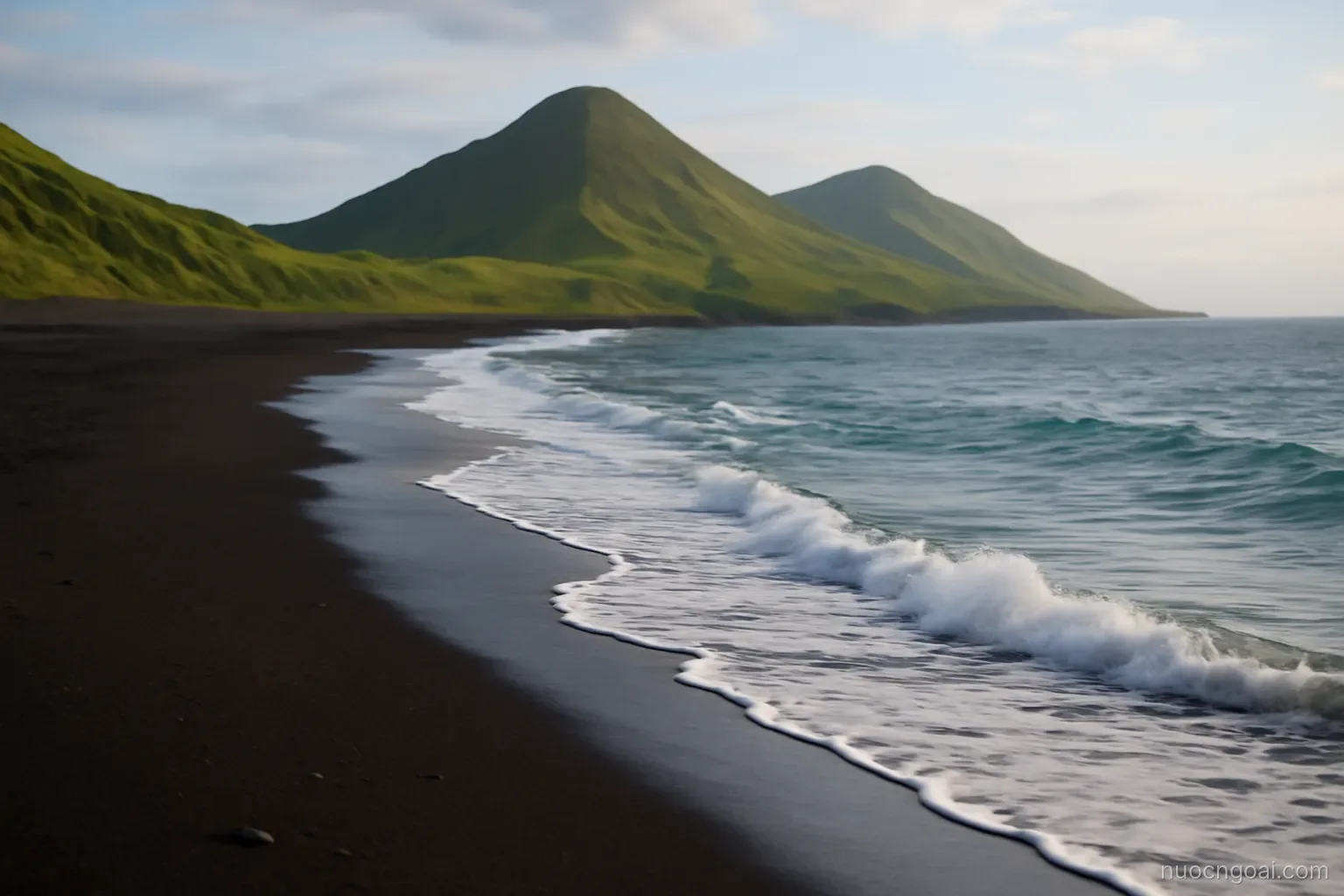 A narrow coastal plain of dark volcanic sand meeting long Pacific swell, green cones inland