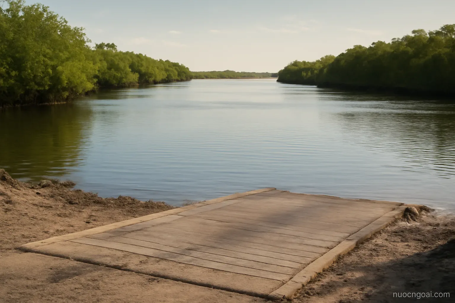 A wide calm river between low mangrove banks with a vehicle ferry ramp cut into the near shore