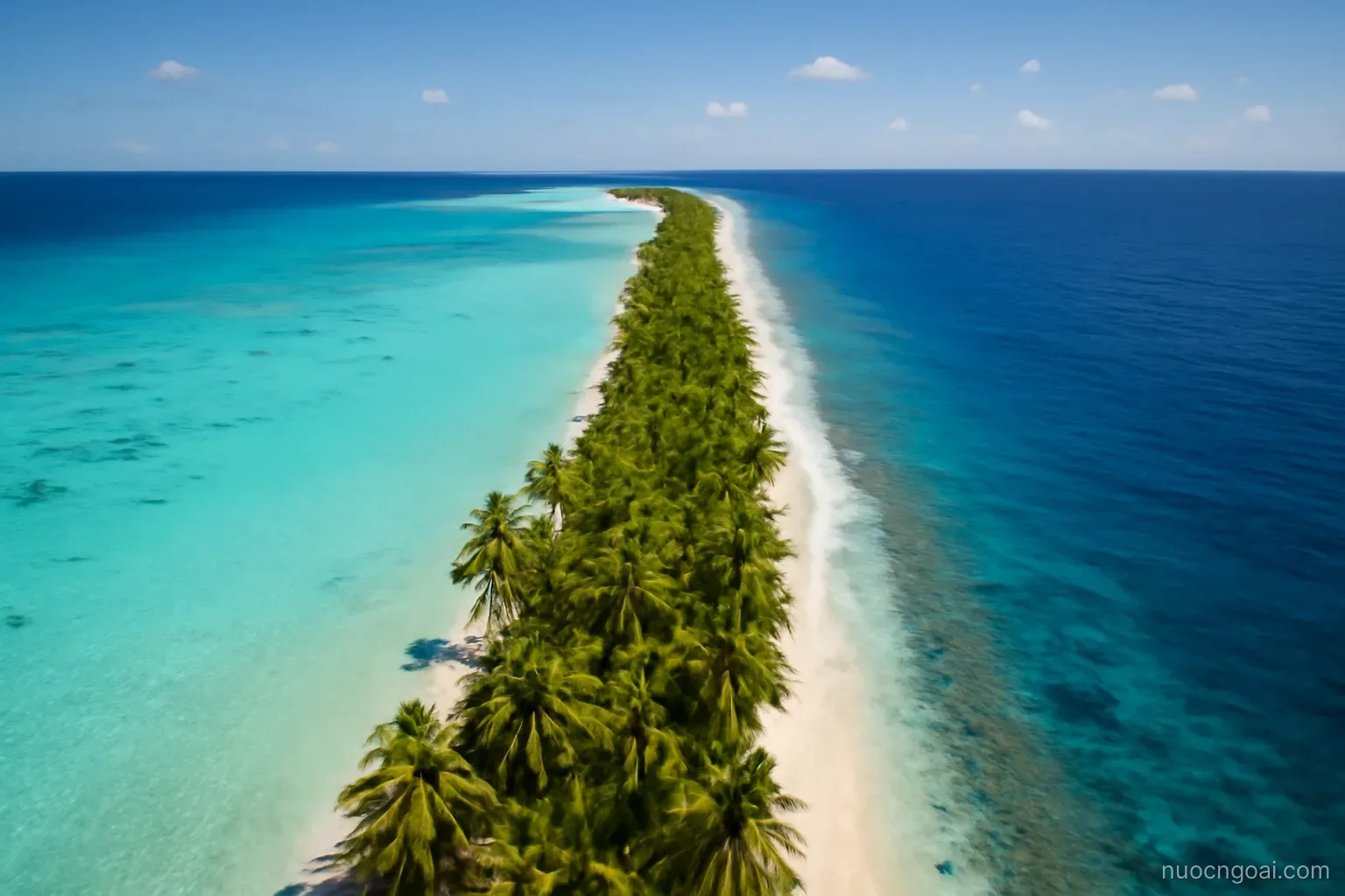 A very narrow strip of palm-covered atoll dividing a turquoise lagoon from deep ocean under high sun