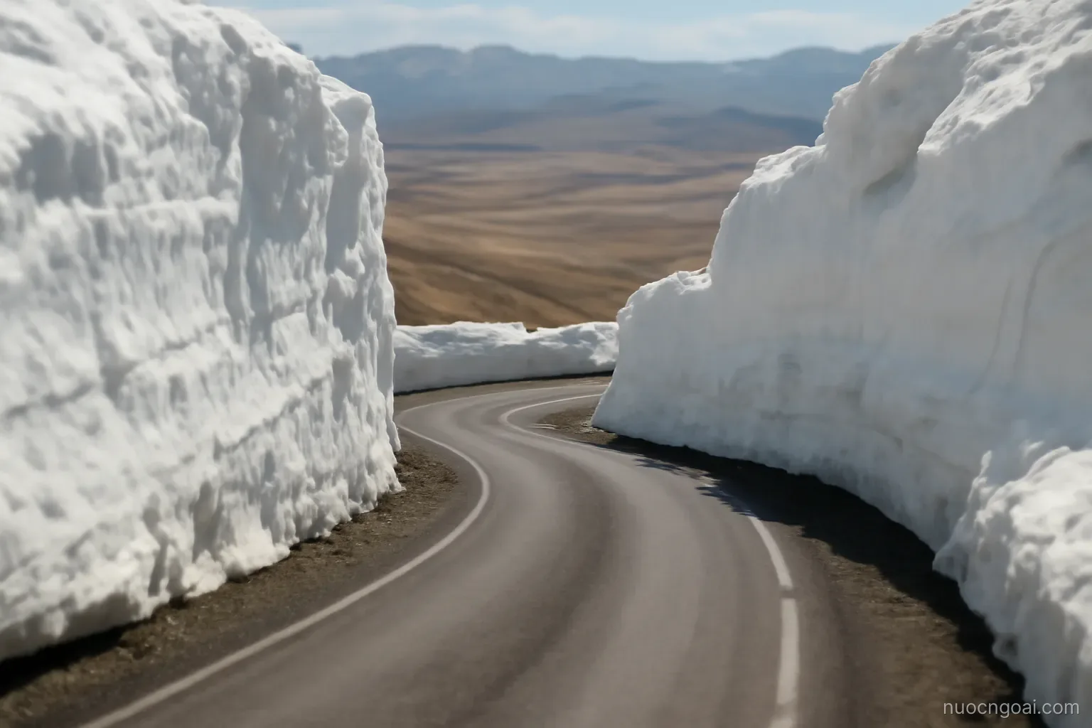 A high pass road switchbacking between snow walls, a valley of pale grassland opening far below