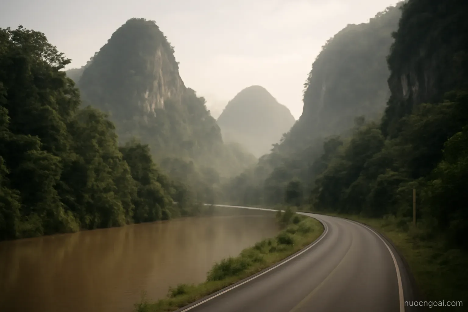 Forested limestone hills rising above a slow brown river, a single road following the valley in hazy light