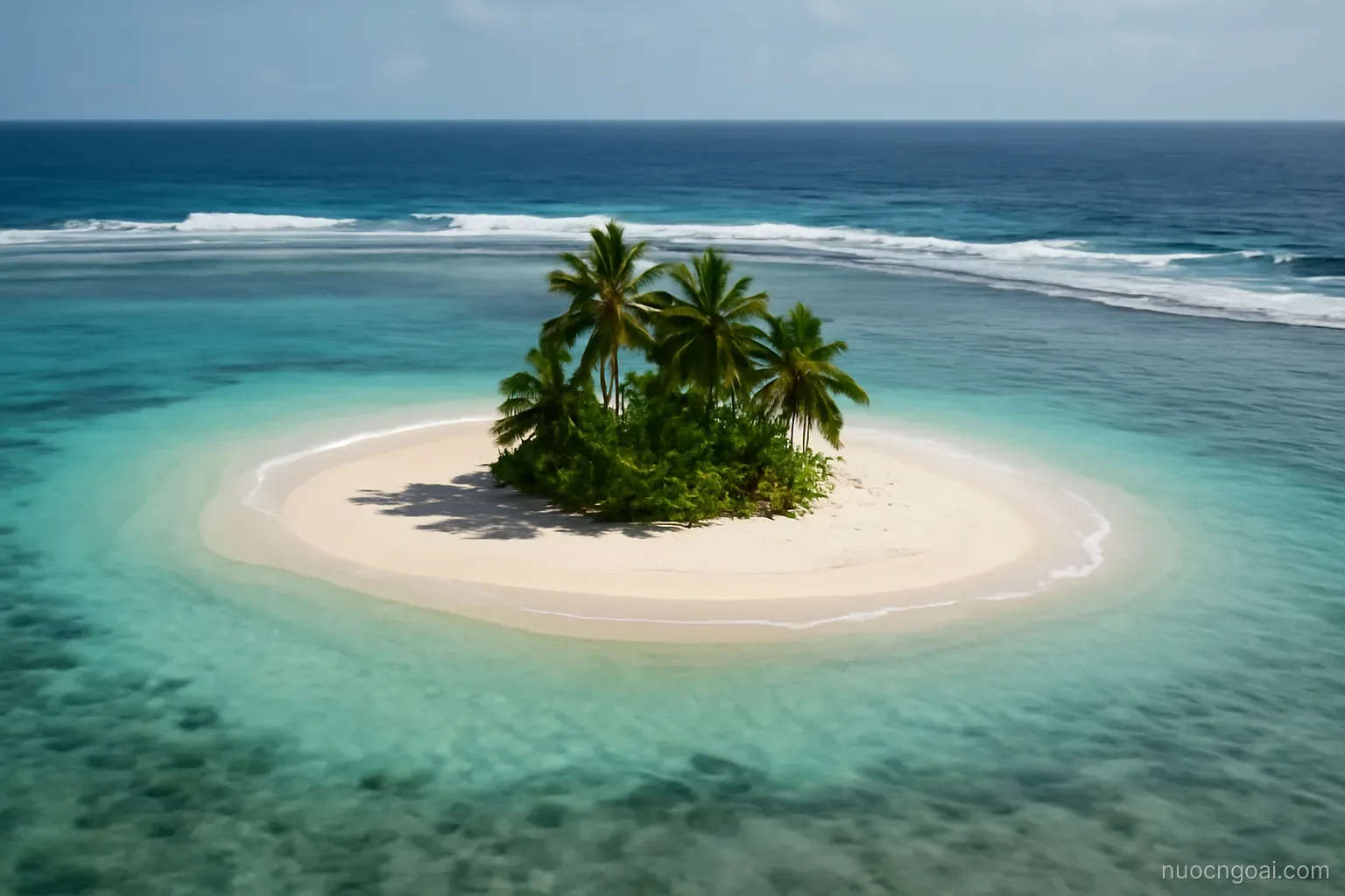 A ring of pale sand and shallow lagoon around a low palm islet, open ocean breaking on the outer reef