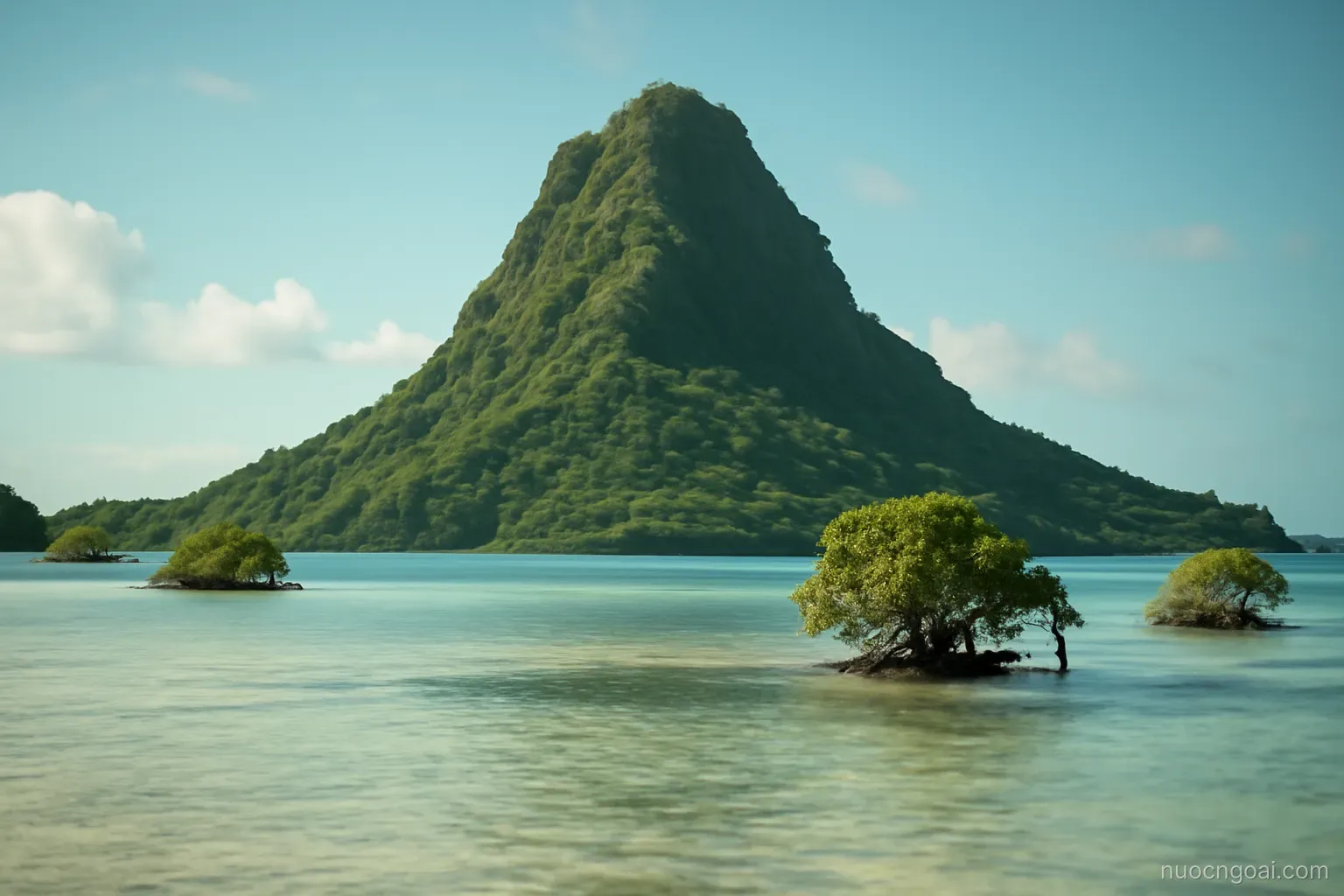 A steep green island rising from a wide reef lagoon with scattered mangrove islets in calm water