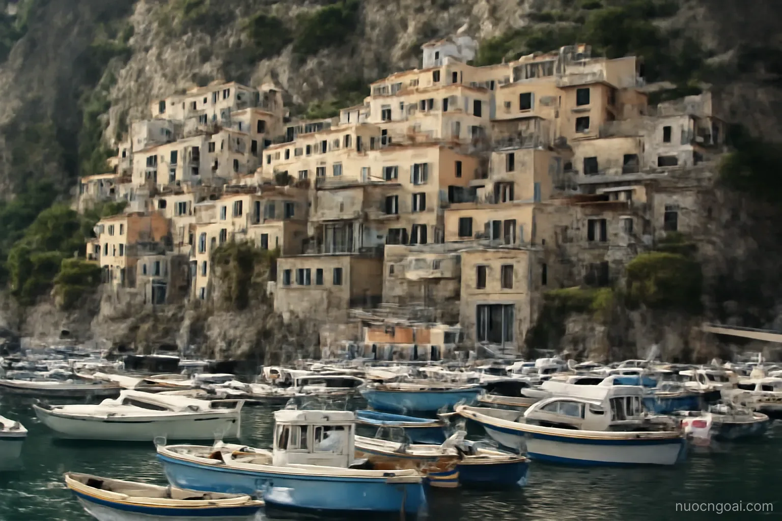 Tiered apartment blocks built into a steep rock face above a harbour crowded with moored boats