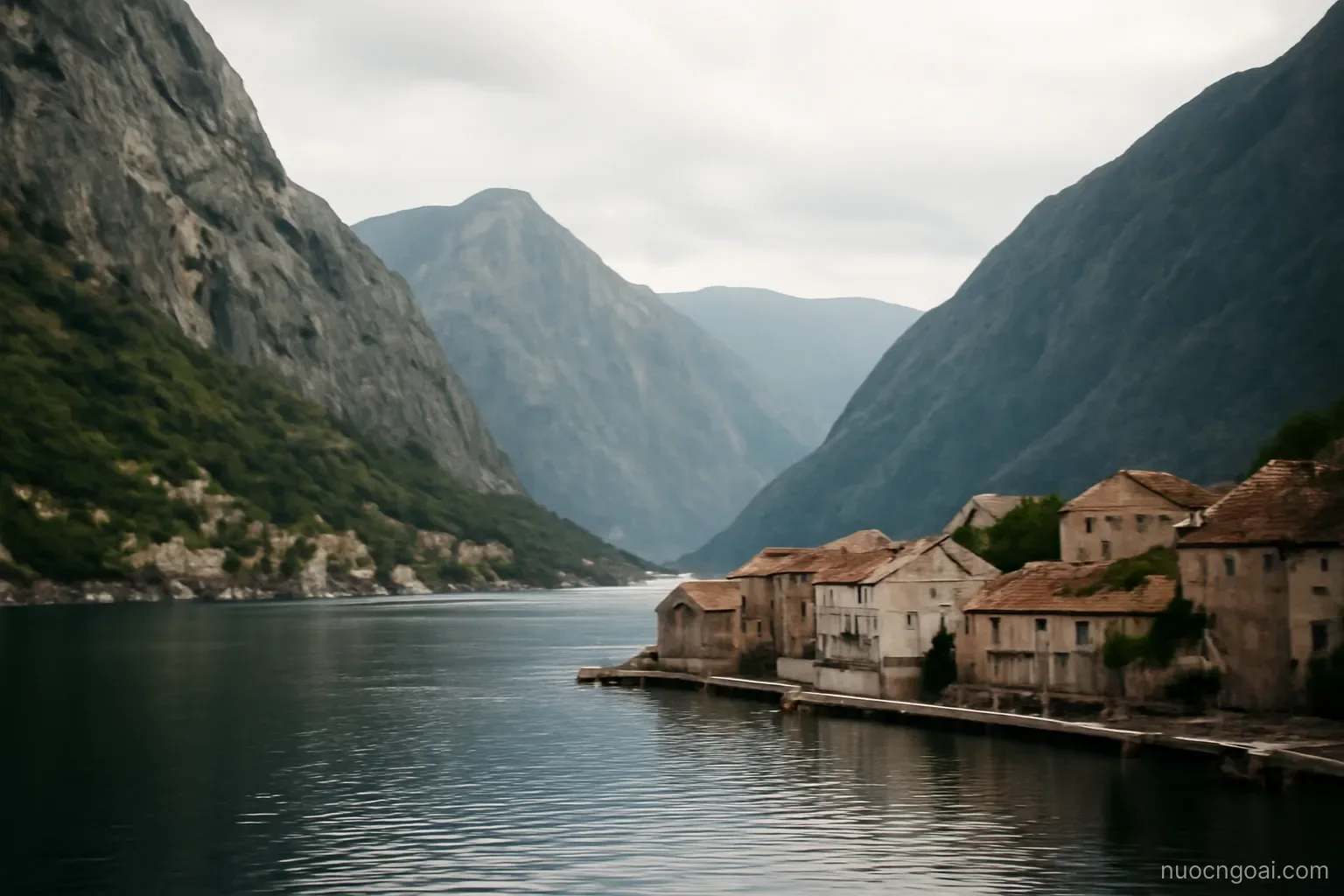 A deep fjord-like bay between steep grey mountains, small stone villages at the waterline