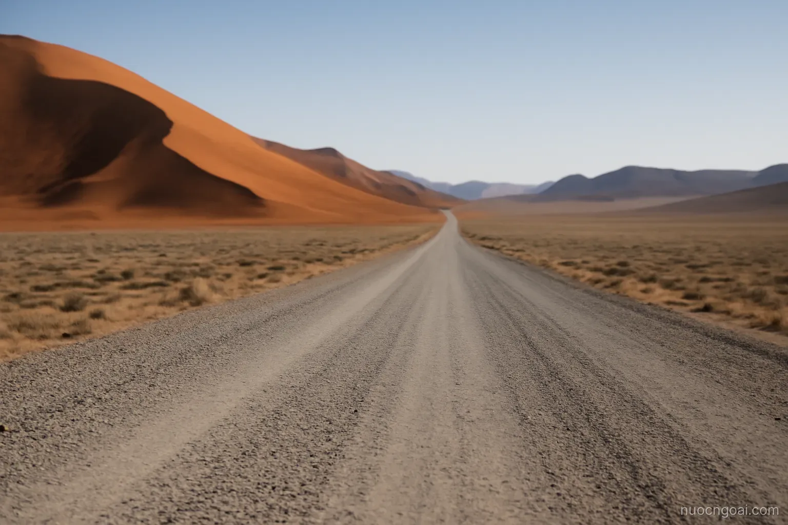 A gravel road running dead straight between red dunes and gravel plain, no vehicles in sight