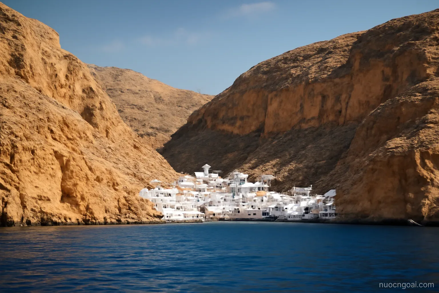 Bare ochre mountains dropping straight into a deep blue sea, a white harbour town in the gap