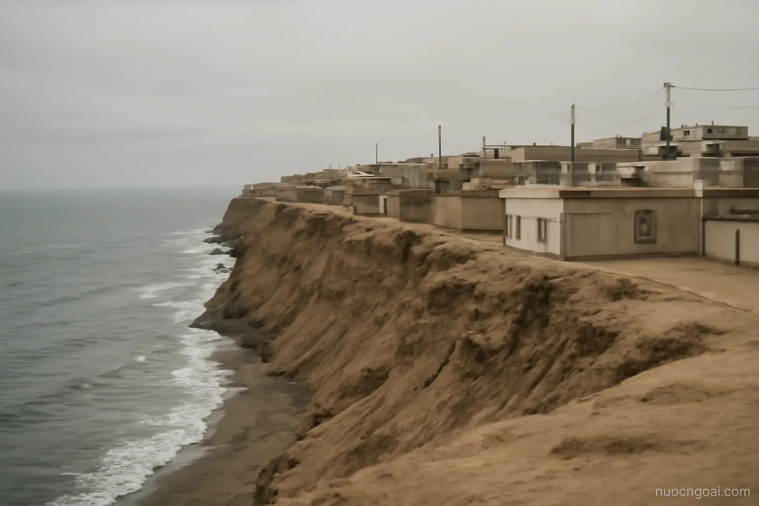 A dry coastal city on sand cliffs above grey ocean, low buildings under a permanent overcast layer