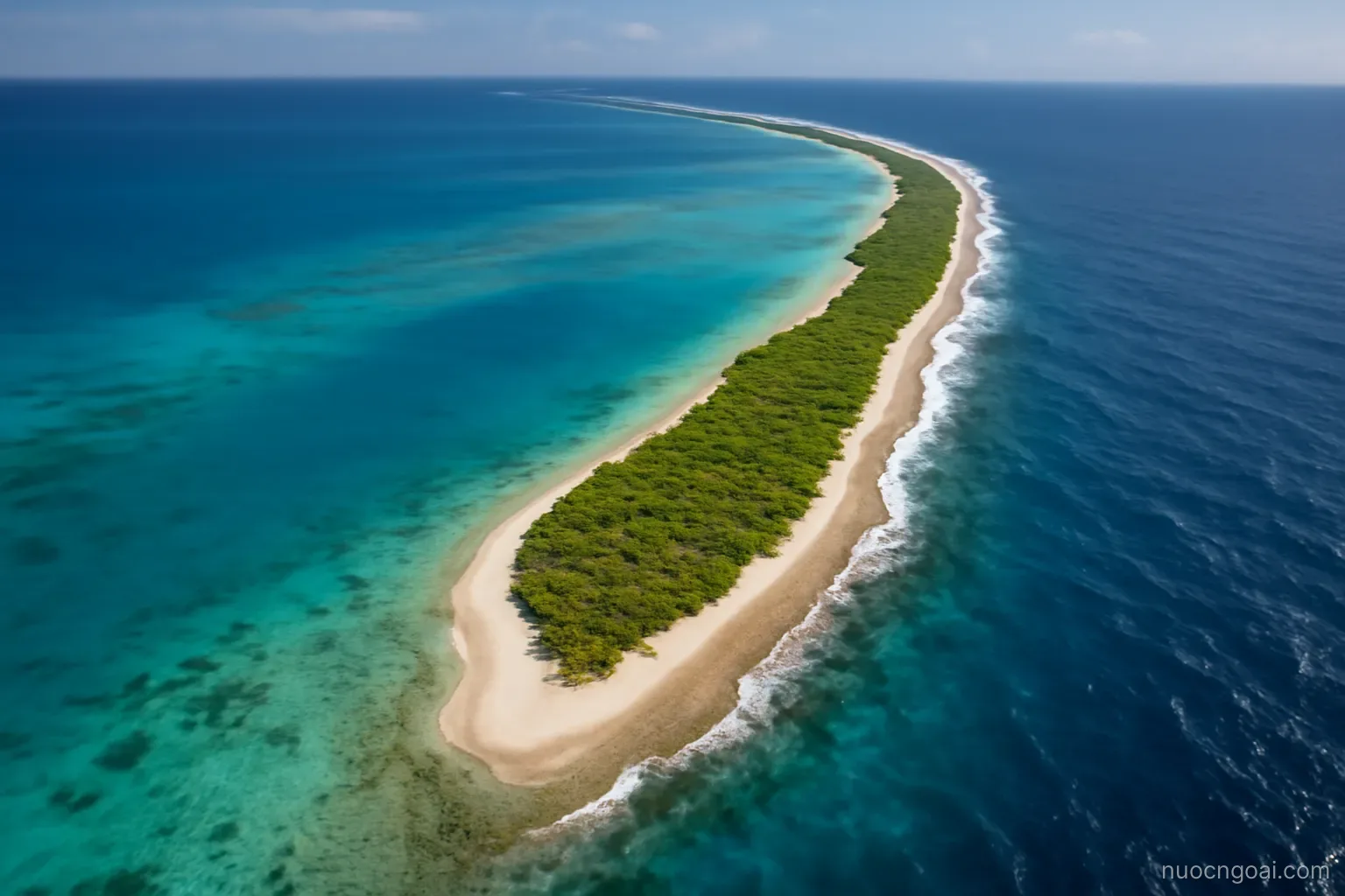 A narrow strip of atoll land between a wide lagoon and open ocean seen from above