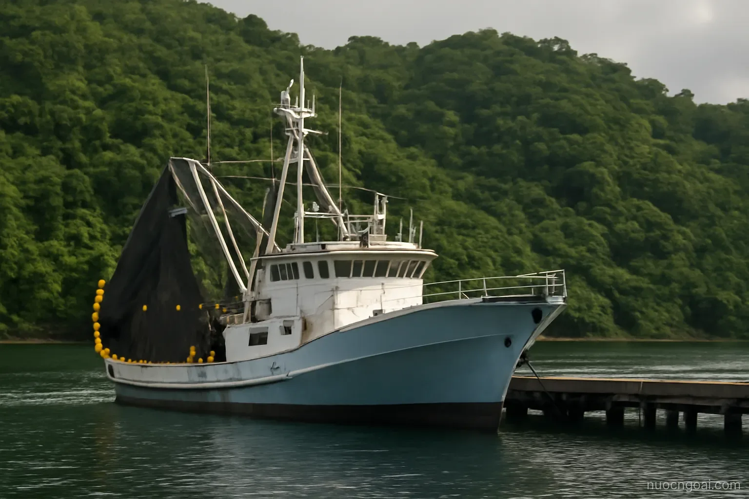 A tuna purse seiner tied alongside a small wharf with dense jungle hills rising directly behind