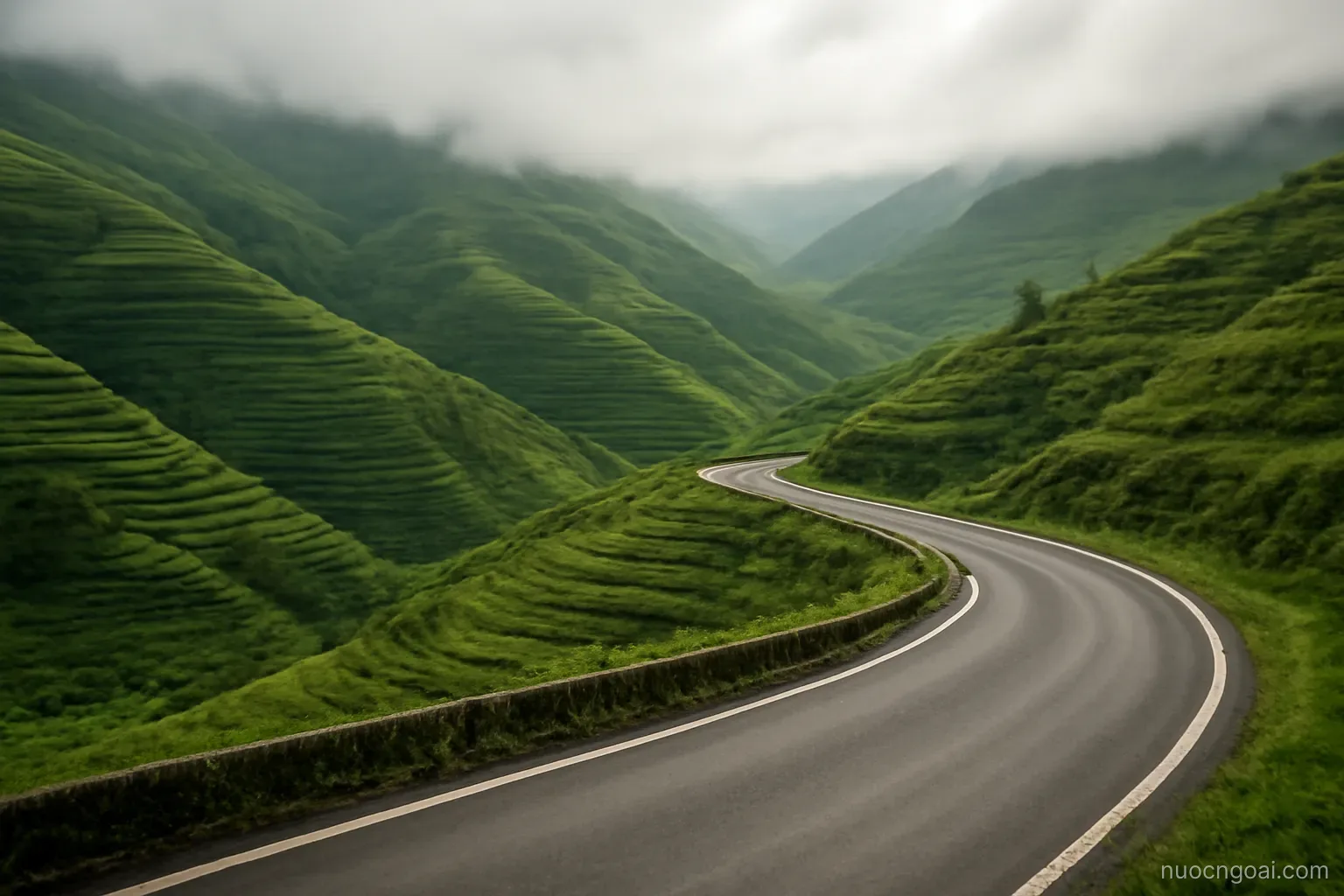 Terraced green hills folding into each other under low cloud, a paved road curving along a ridge