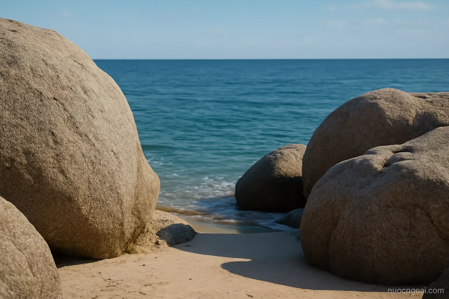 Granite boulders on a narrow beach with deep blue open ocean stretching unbroken to the horizon