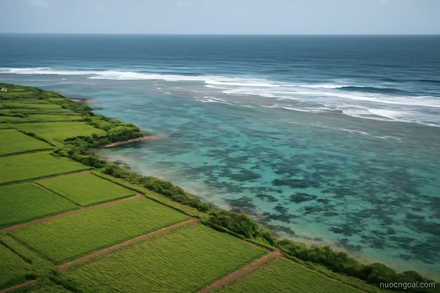 A low coral coastline of flat green plantations with a shallow reef lagoon and breaking surf beyond