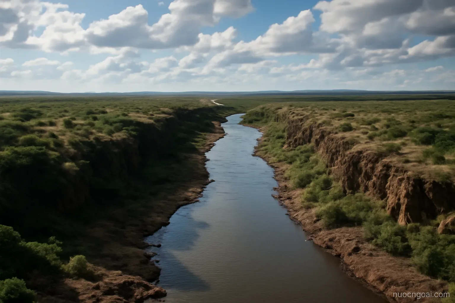 A broad river above a gorge, low bush stretching to the horizon under building afternoon clouds