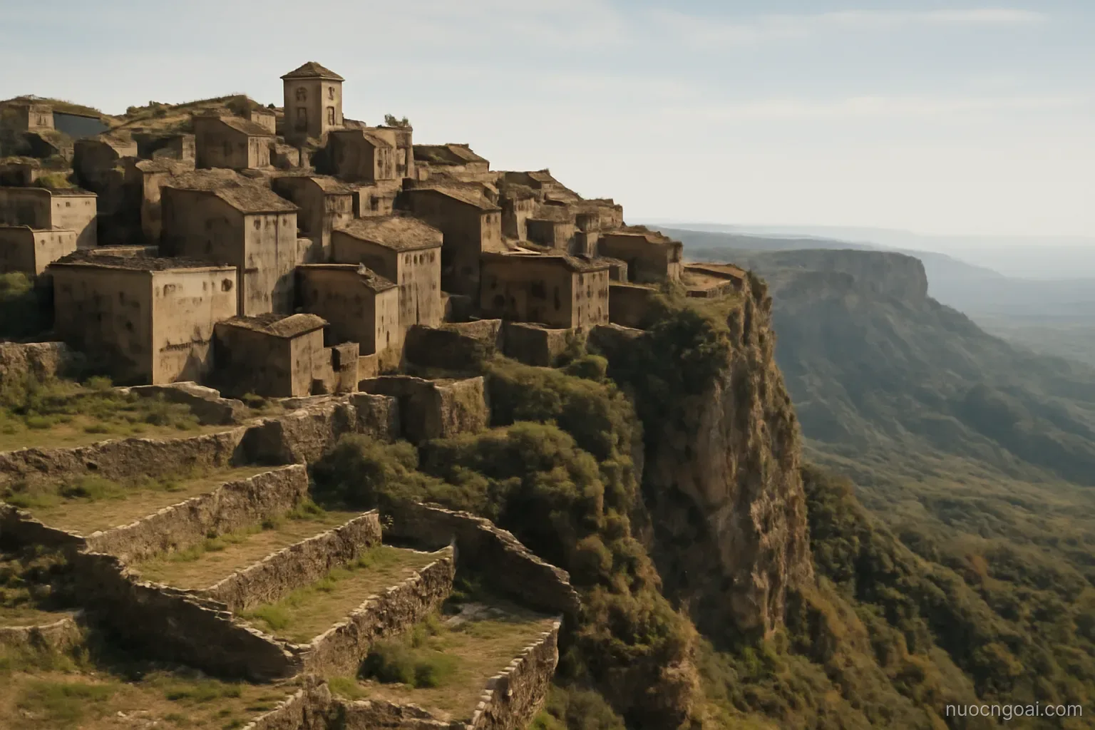 A highland plateau town of stone terraces with a long escarpment dropping toward distant coastal haze