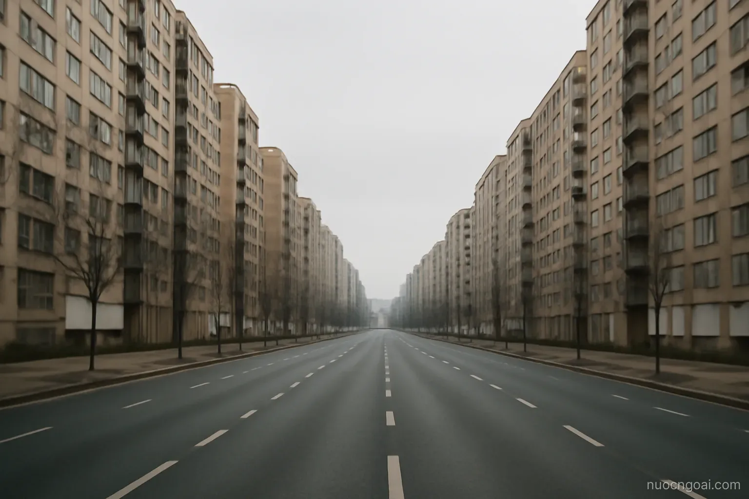 A wide empty boulevard lined with tall uniform apartment blocks stretching away under flat overcast light