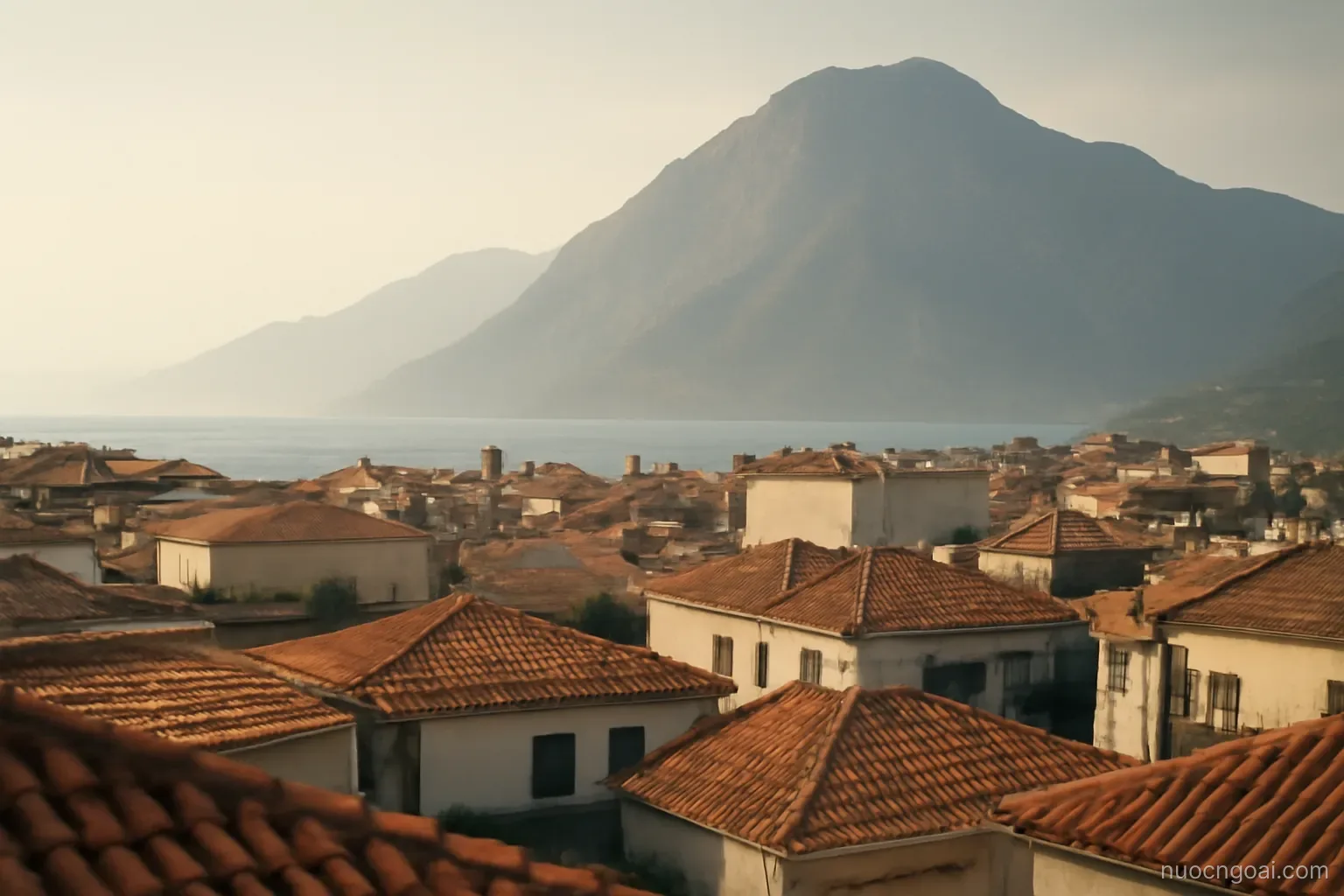A coastal range rising abruptly behind a low city grid, hazy afternoon light over tiled rooftops